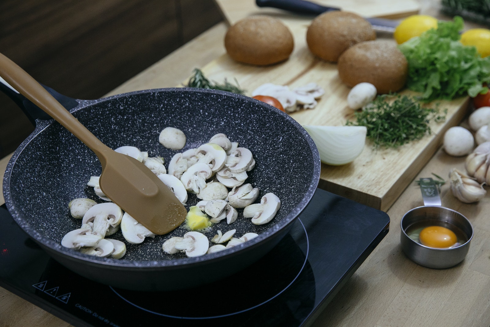 Chopped mushrooms in frying pan placed on stove near various veggies and herbs